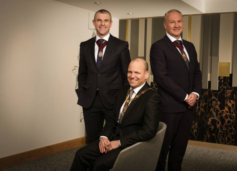 Three men in various positions of sitting and standing wearing presidential chains and medallions