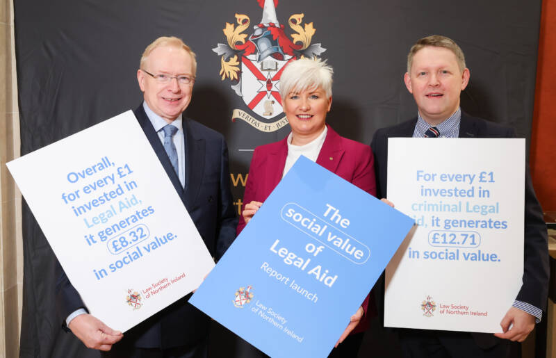 3 individuals holding placards representing the launch of the social value of Legal Aid report. Law Society of Northern Ireland CEO David Lavery, MLA and Chair of the Justice Committee Joanne Bunting, Law Society of Northern Ireland Council member Joe McVeigh