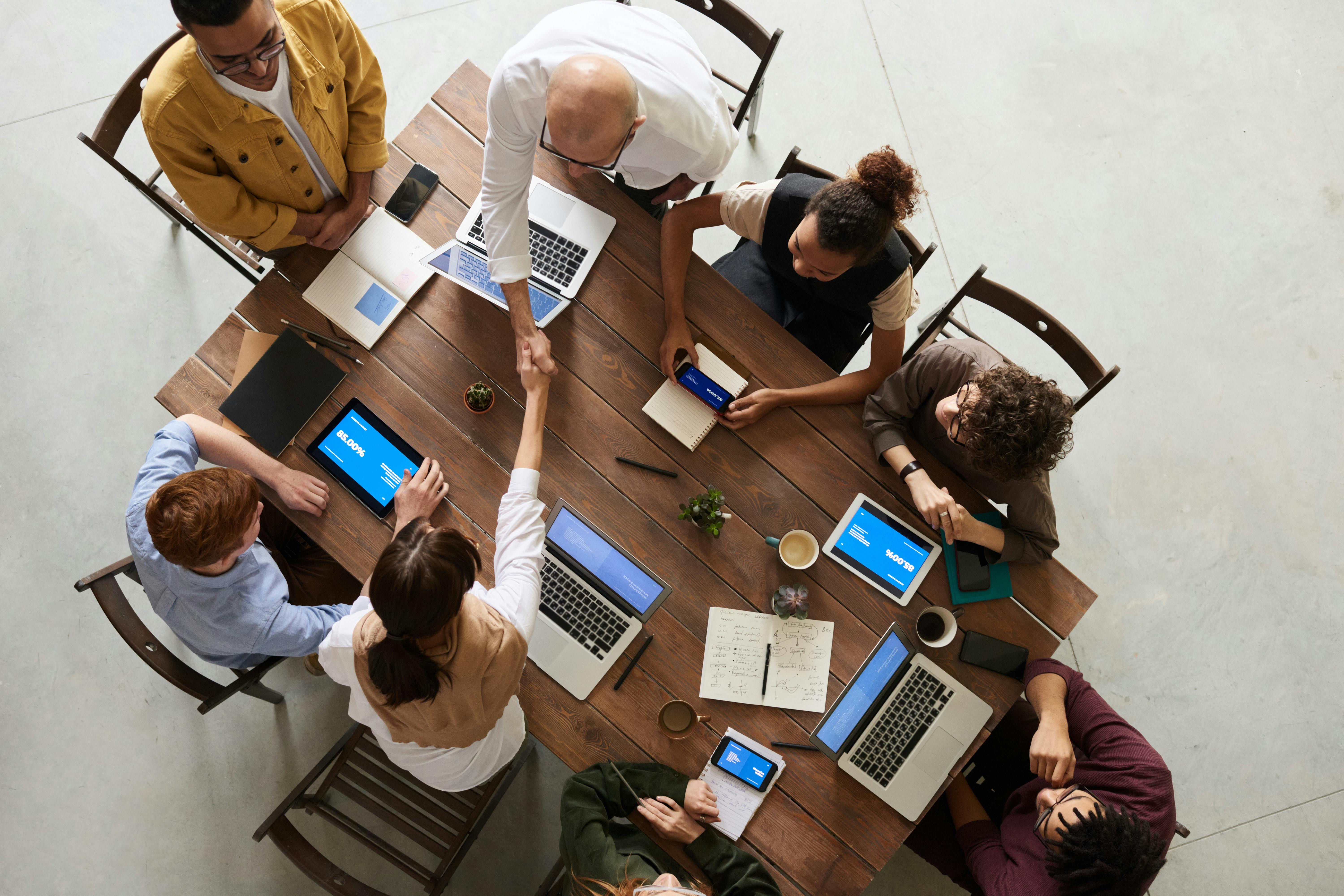 Several people working on computers at a table, two of which are shaking hands
