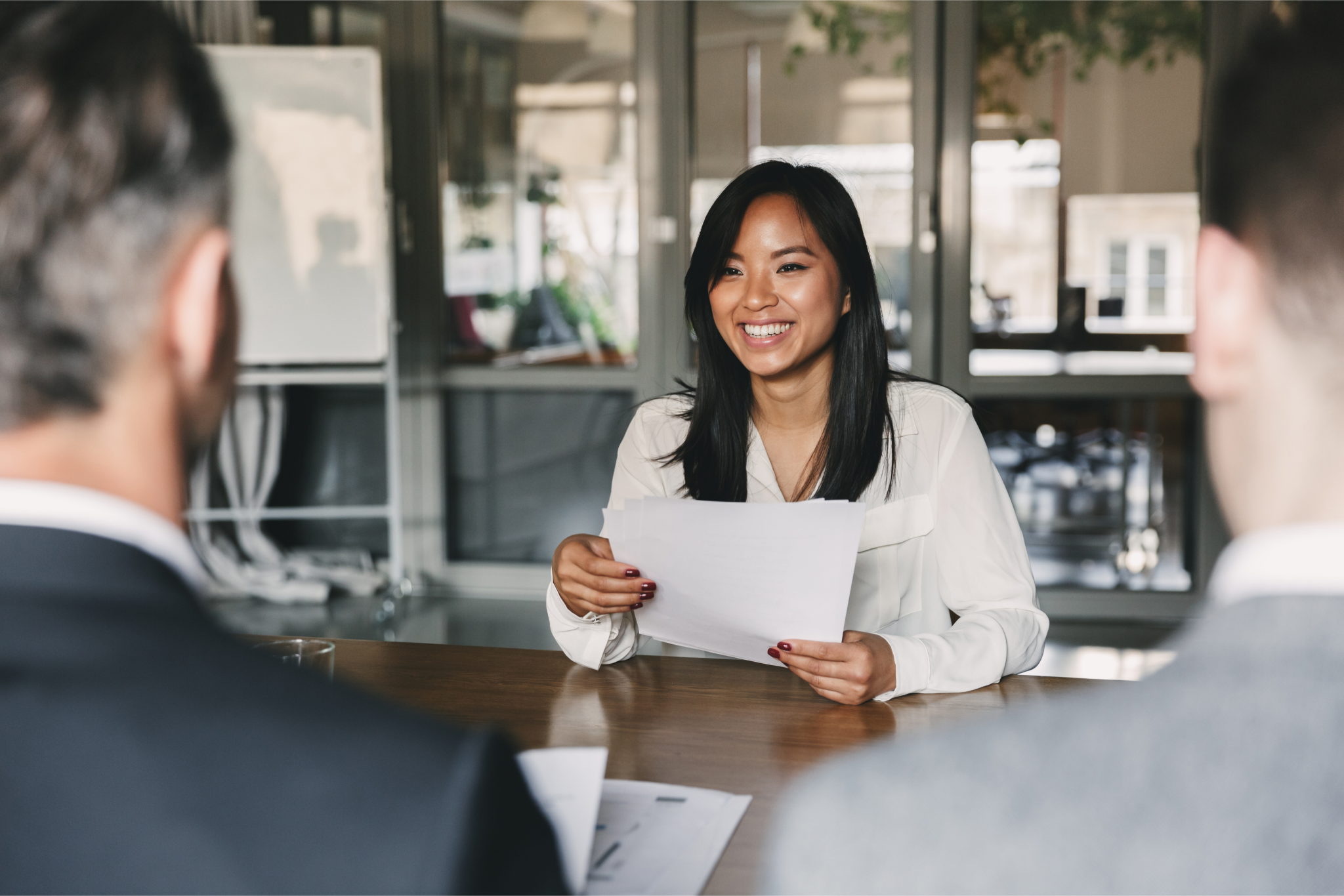 Woman smiles at people across a table while holding papers