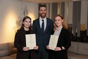 3 people standing indoors, 2 holding certificates