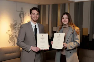 2 people standing indoors holding certificates